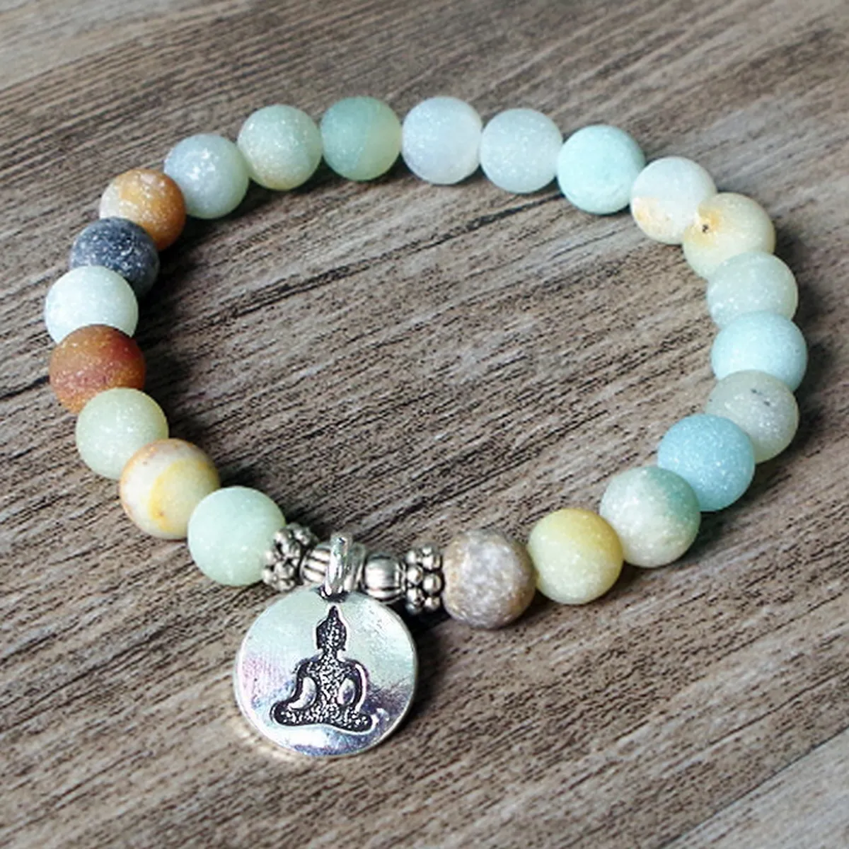 Bracelet en perles d’amazonite avec médaille bouddha, posé sur un plateau en bois