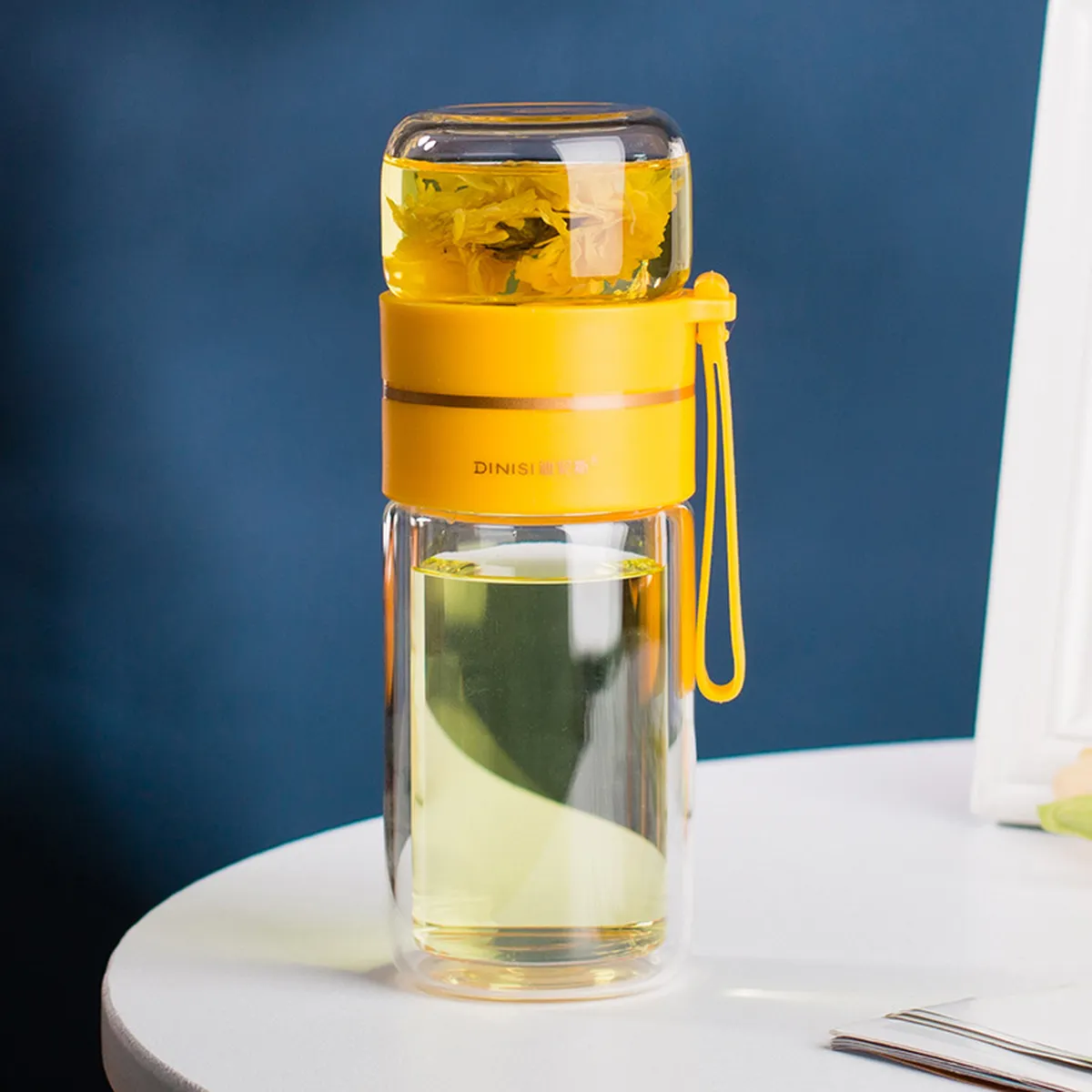 Gourde à thé en verre jaune remplie d’infusion, sur une table
