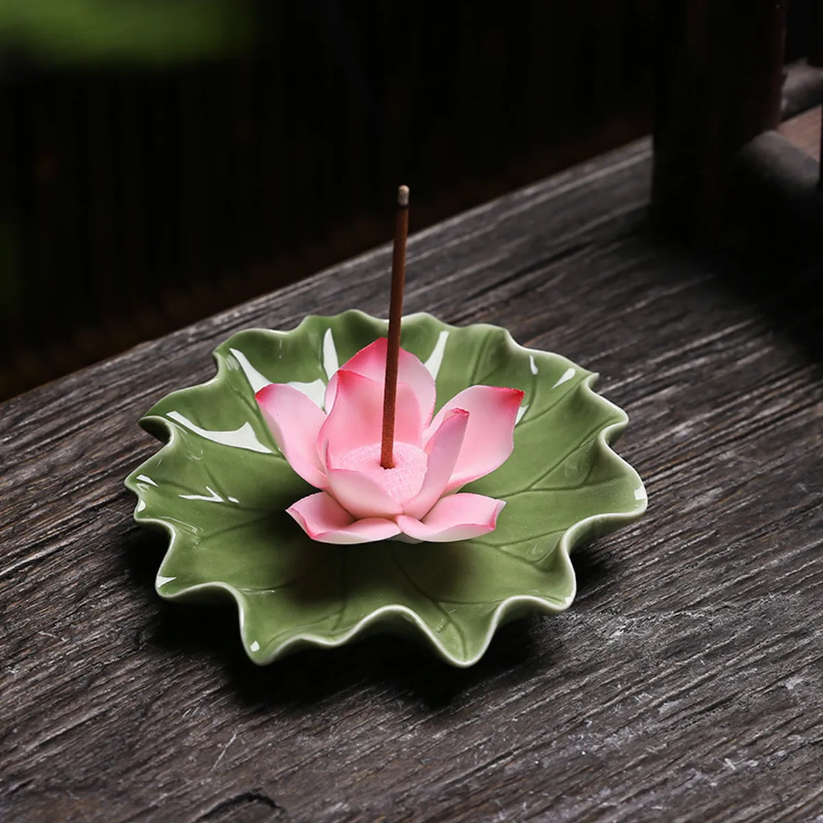 Porte-encens lotus rose sur sa feuille verte, un bâton planté, sur une table sombre