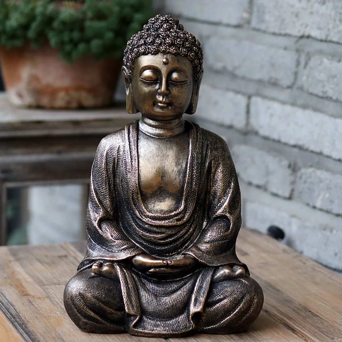 Statuette de bouddha en méditation posée sur une table en bois, devant un mur de briques