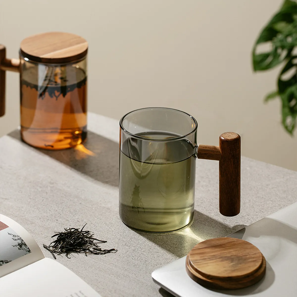 Tasses en verre ambré et gris teinté avec couvercle en bois, feuilles de thé à côté