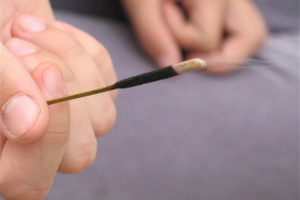 Un bâton d’encens allumé tenu entre les doigts